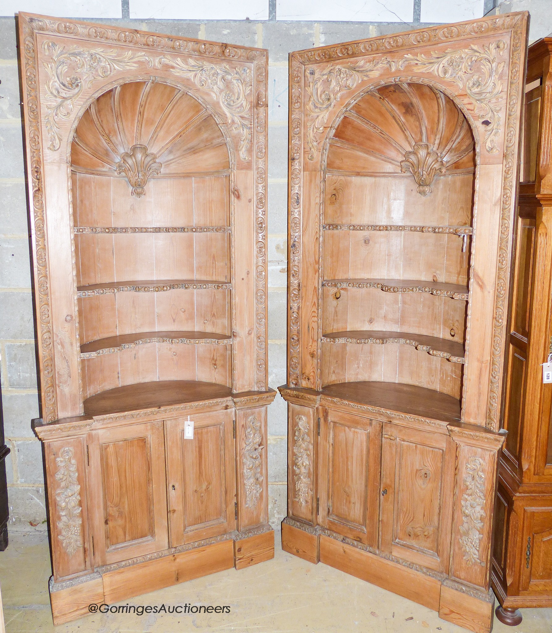 A pair of George III style carved stripped pine niche barrel back open corner cupboards, width 90cm, depth 40cm, height 208cm